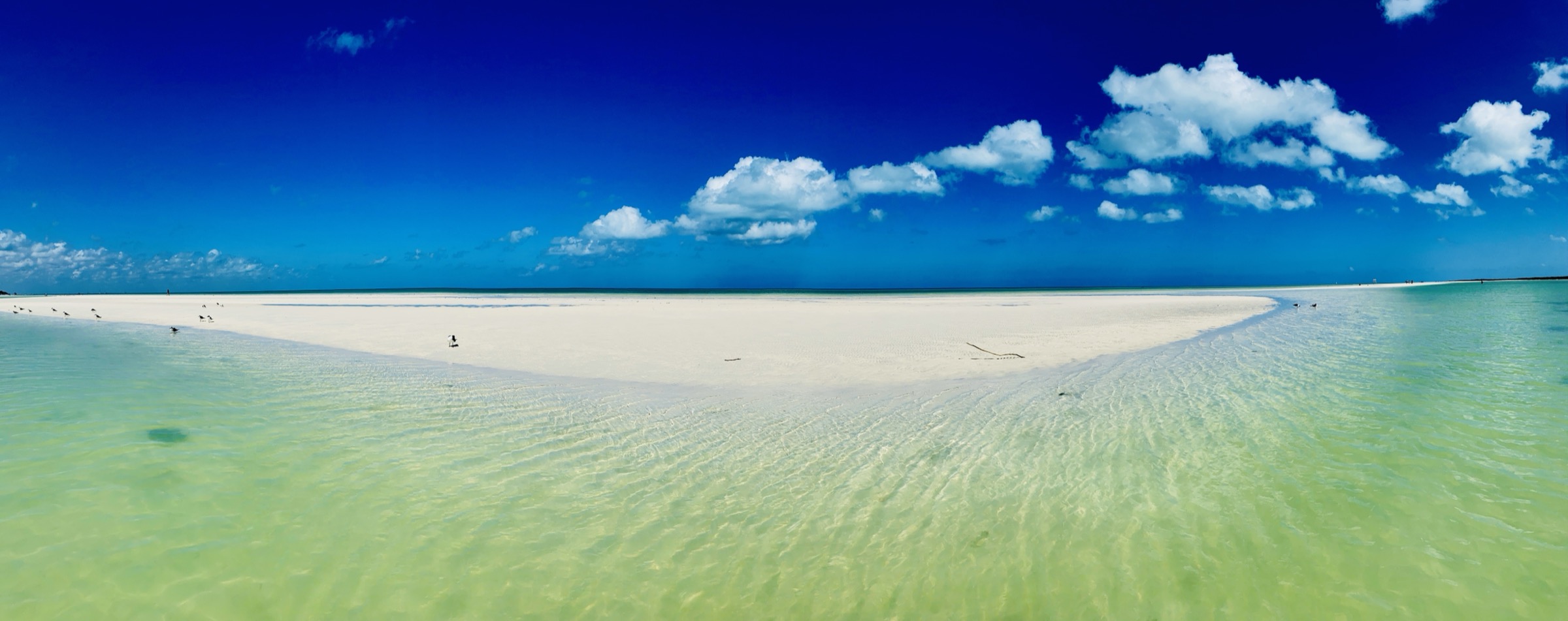 A white sand spit surrounded by turquoise shallow water under a bright blue sky