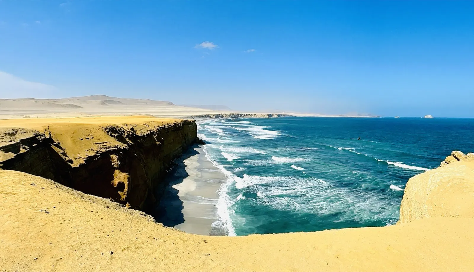 Golden desert cliffs meeting a turquoise ocean, with waves breaking along an empty beach