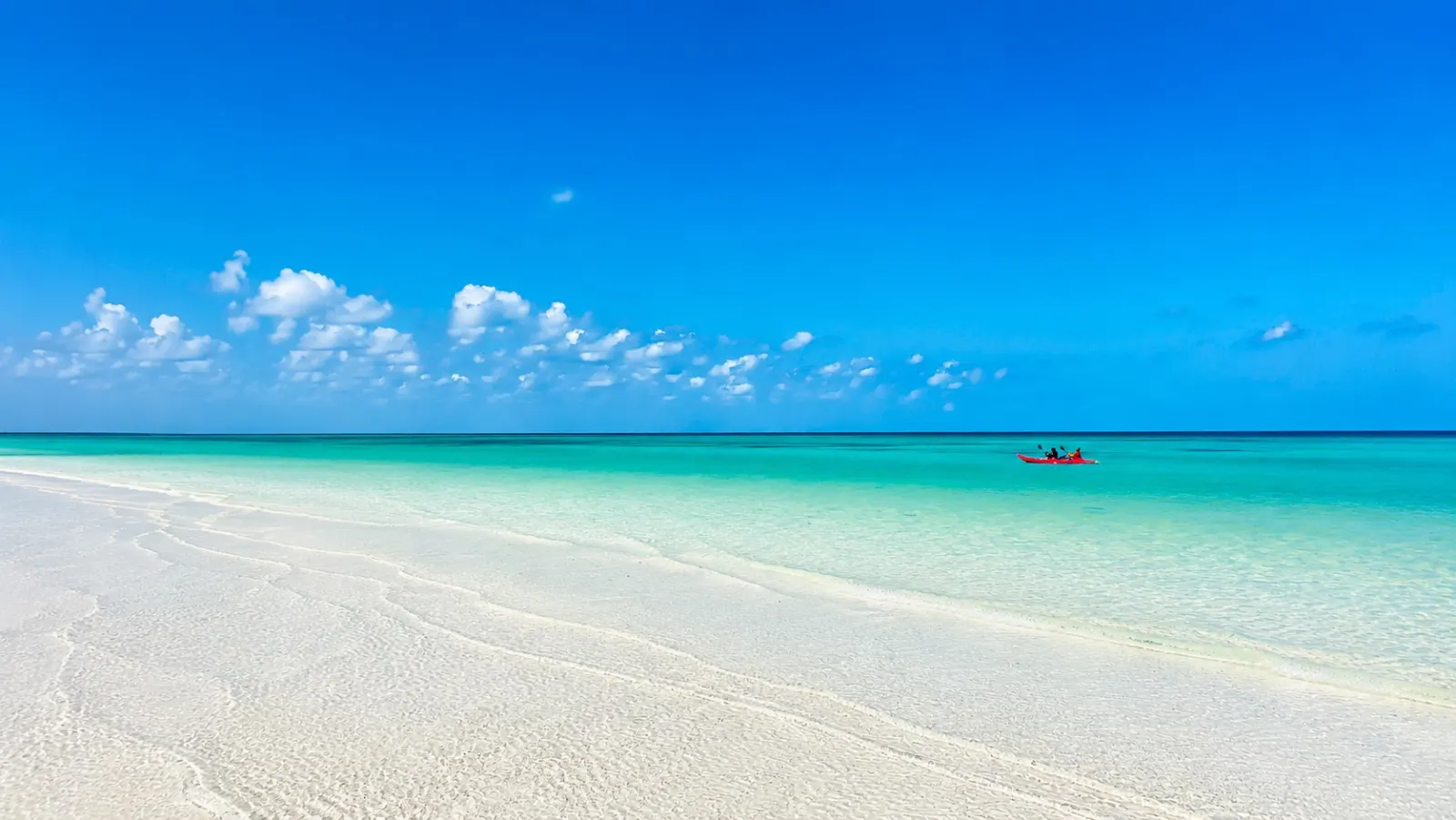 A red kayak on turquoise shallows off the wide white-sand beach at Holbox, Mexico