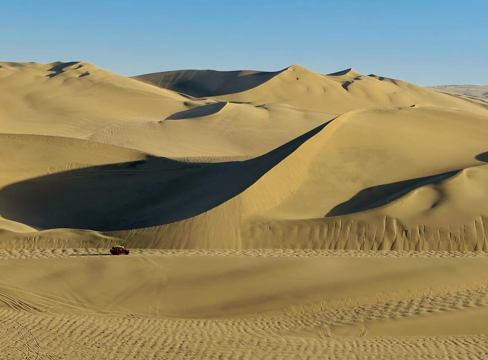 A lone buggy crossing vast golden sand dunes near Huacachina, Peru