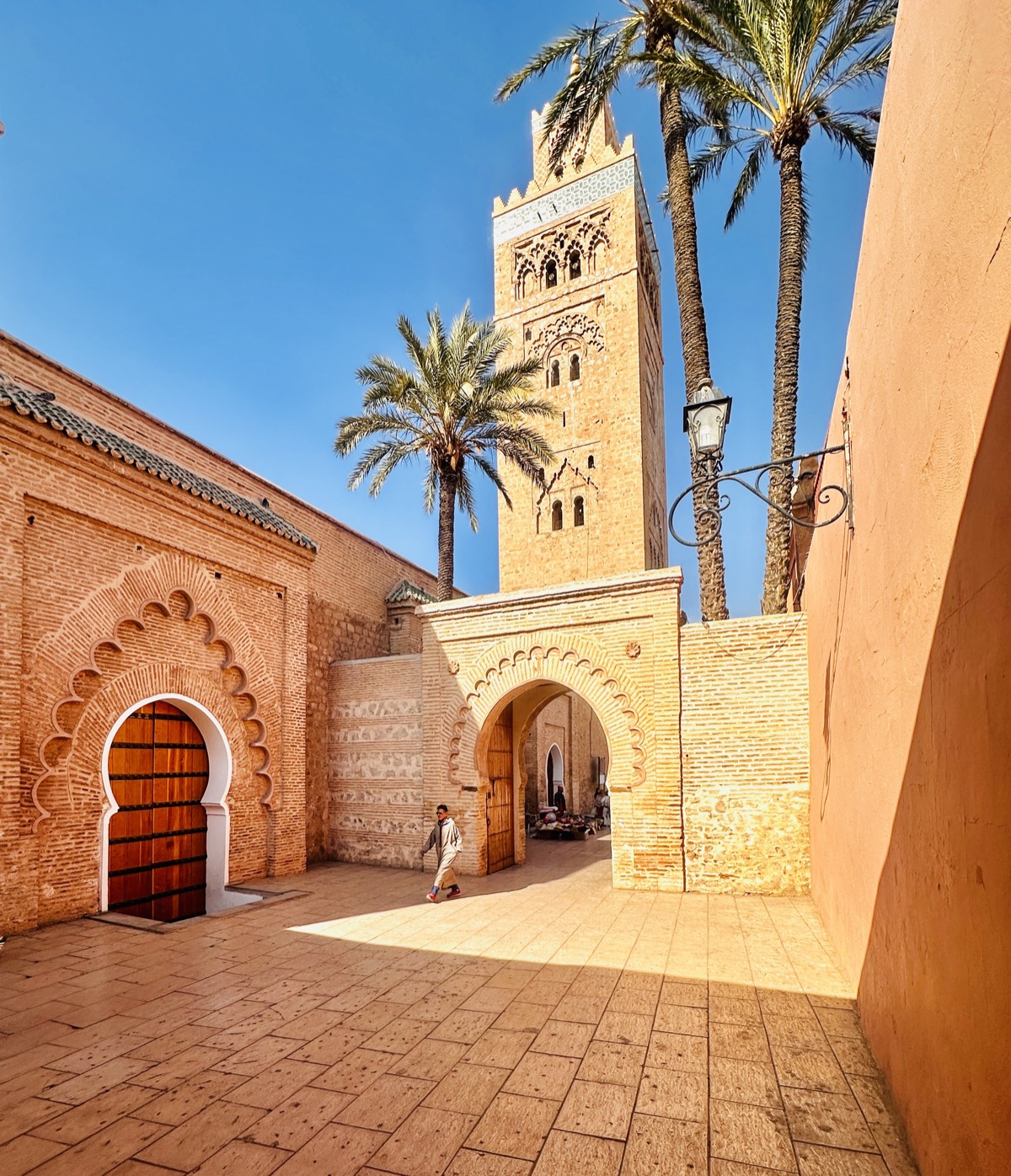 A carved archway gate in Marrakech with the Koutoubia Mosque minaret and palm trees behind it