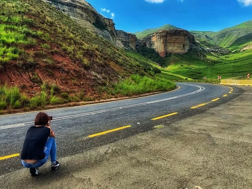 Monica crouching to photograph a winding road through the sandstone cliffs of Golden Gate, South Africa